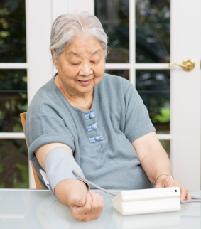 Picture of elderly asian woman taking her own blood pressure at a table