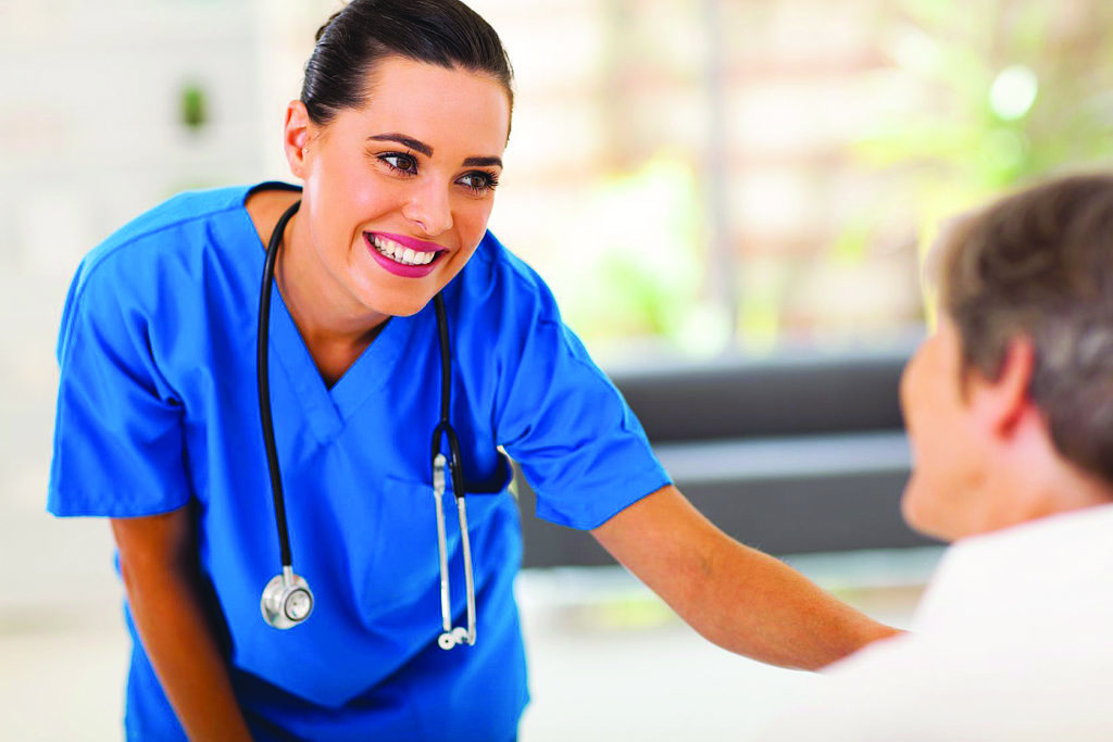 Young nurse in blue scrubs leaning over and speaking with an elderly woman. the elderly woman is looking away