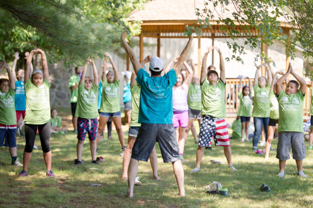 Camp BraveHeart Kids exercising in green tshirts at camp braveheart as a counselor in a blue shirt leads them