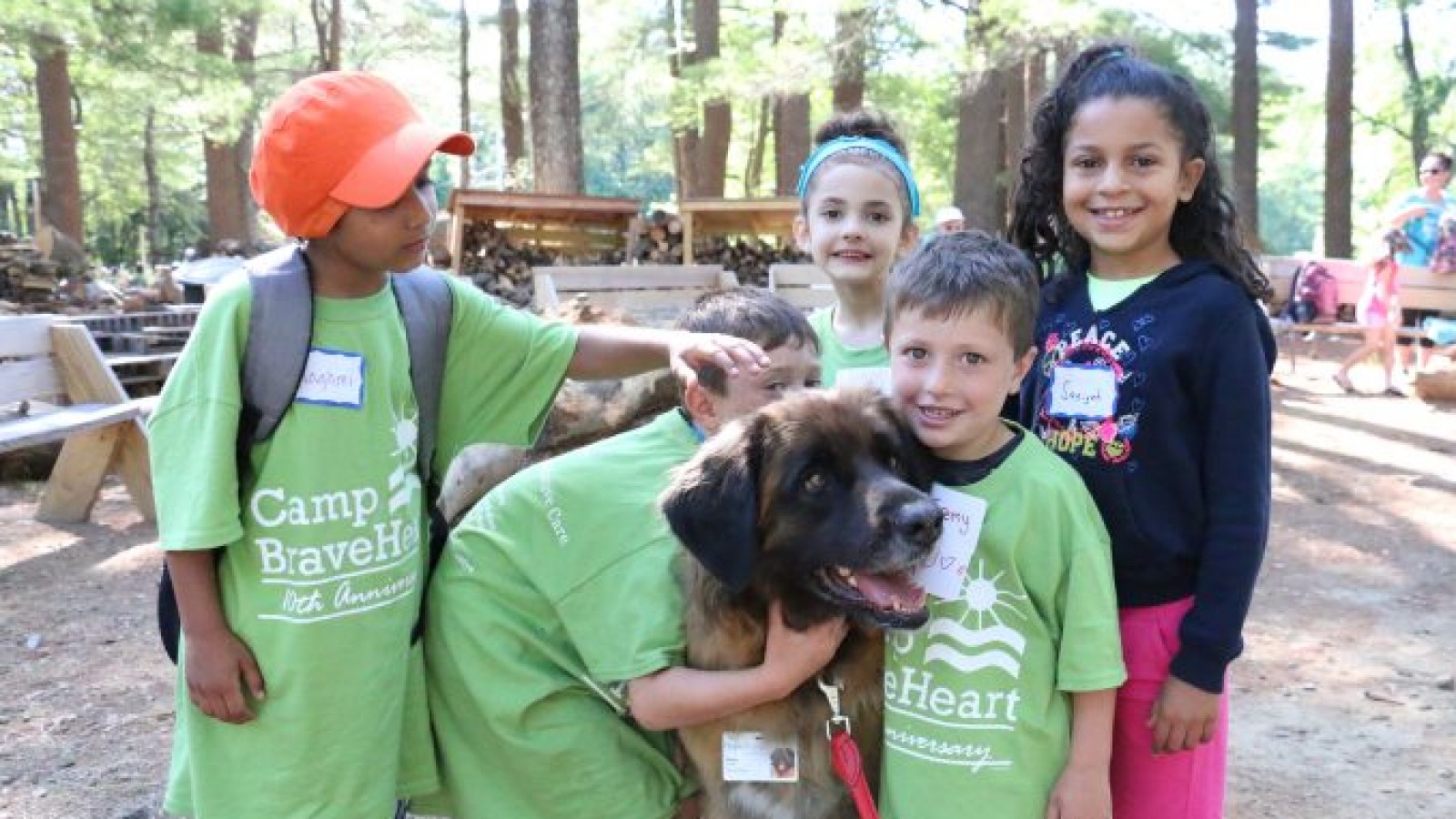 Five kids in green Camp Braveheart shirts smiling while petting dog