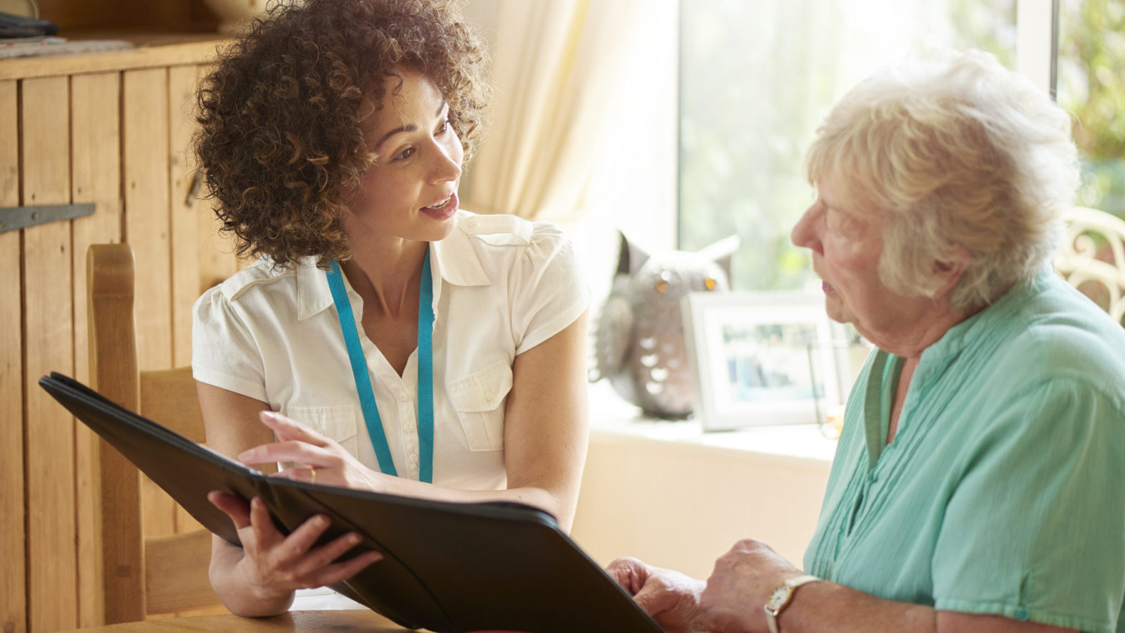 a care worker or medical professional or housing officer makes a house call to a senior client at her home . She is discussing the senior woman’s options on her digital tablet.