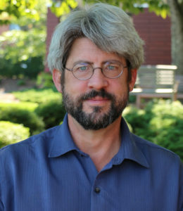 Man wearing blue button up shirt and glasses stands in garden