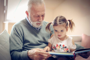 Happy grandfather and granddaughter reading book together at home. Close up.