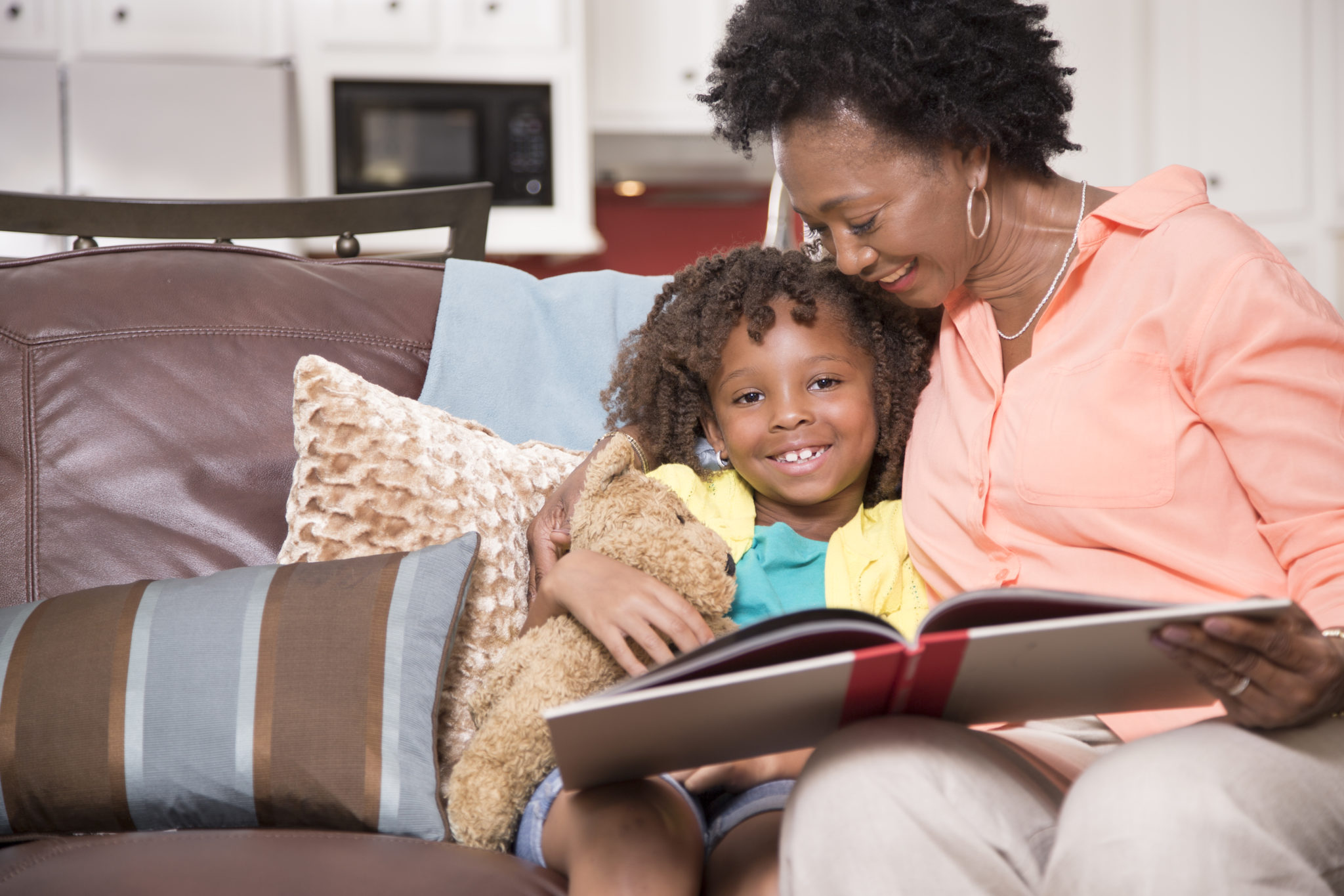 Little girl and mother or grandmother reading books together at home. Kitchen seen in background.