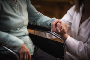 Nurse with senior woman at home, holding hands.