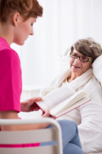 Female nurse reading book to senior patient