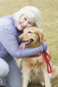 Senior woman (60s) at park with Golden Retriever.