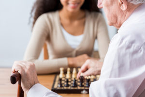 Close-up of older man's hand with walking stick. Man playing chess with young caregiver
