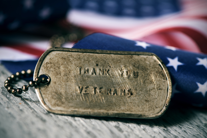 text thank you veterans in a dog tag closeup of a rusty dog tag with the text thank you veterans engraved in it, next to a flag of the United States, on a rustic wooden surface