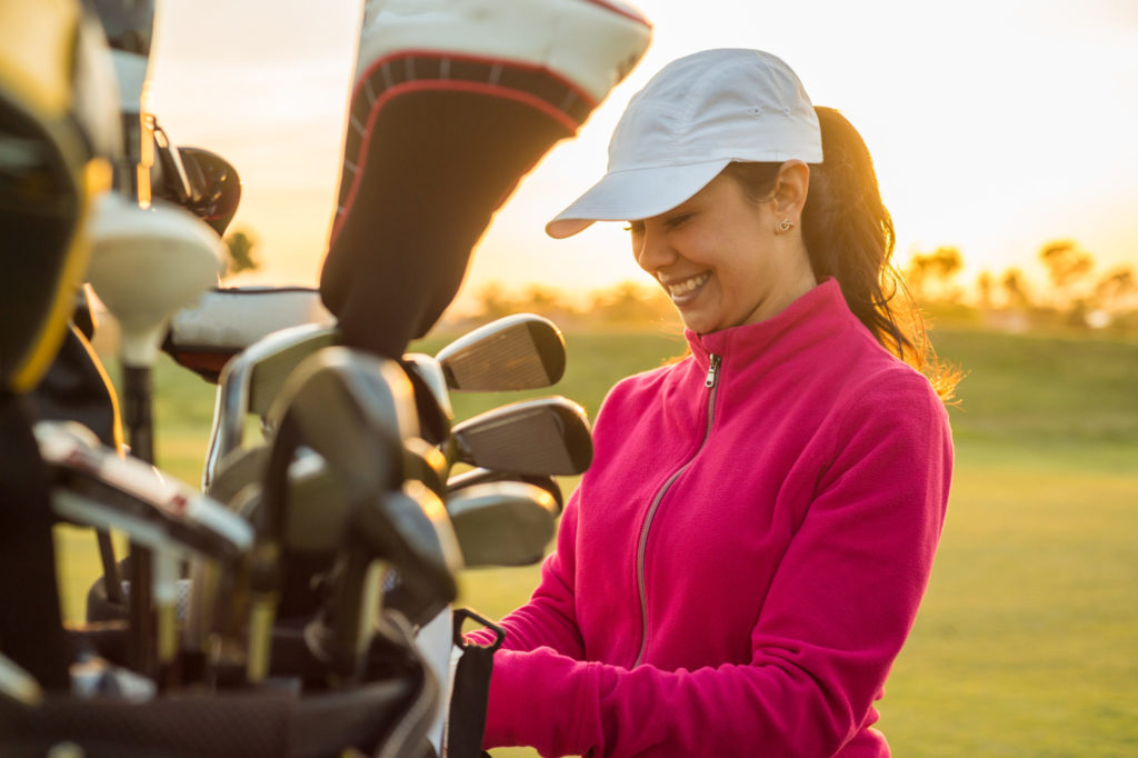Female Golfer Grabbing clubs out of her golf bag at sunset.