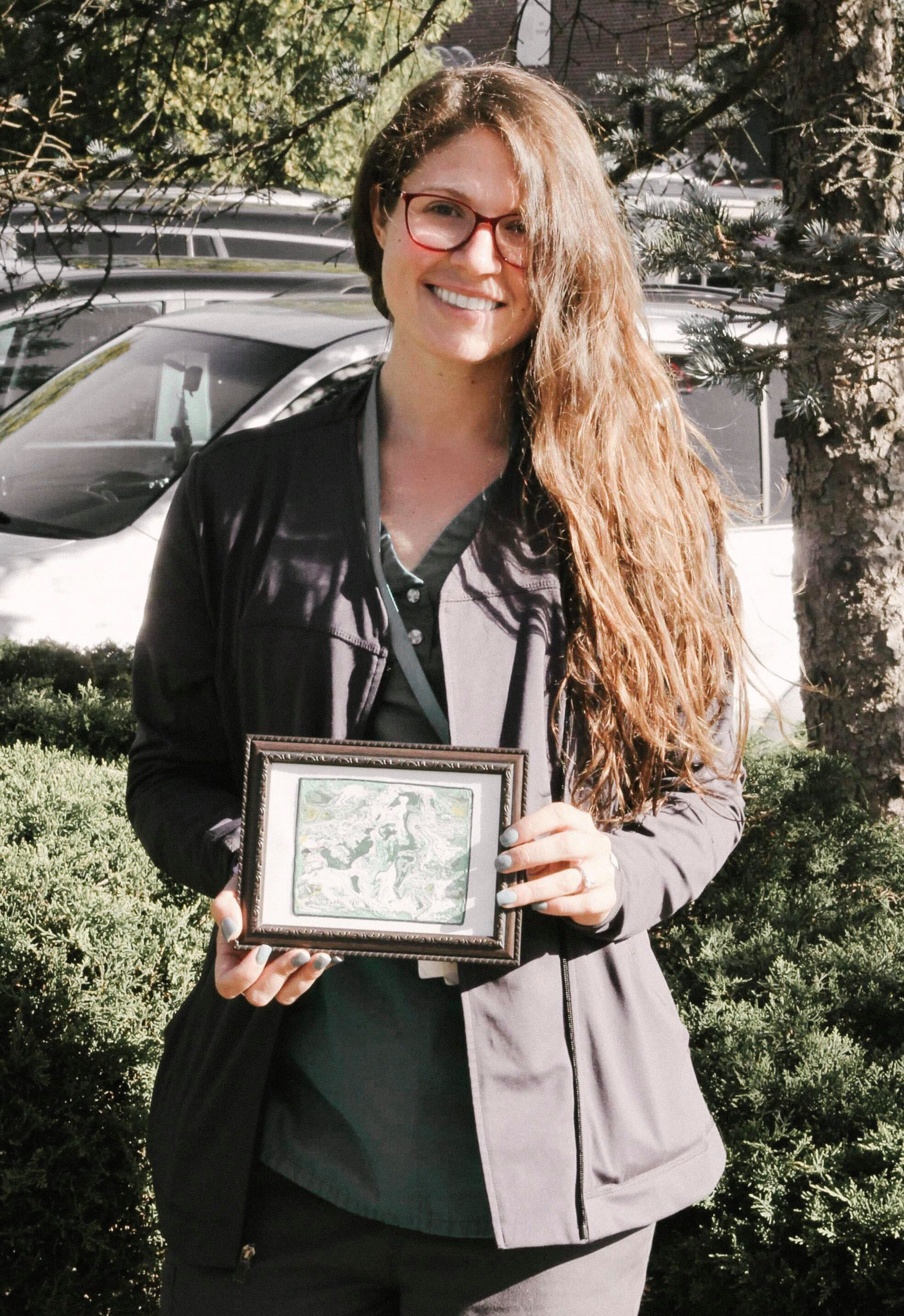 Nurse wearing grey scrubs smiles while holding a painting