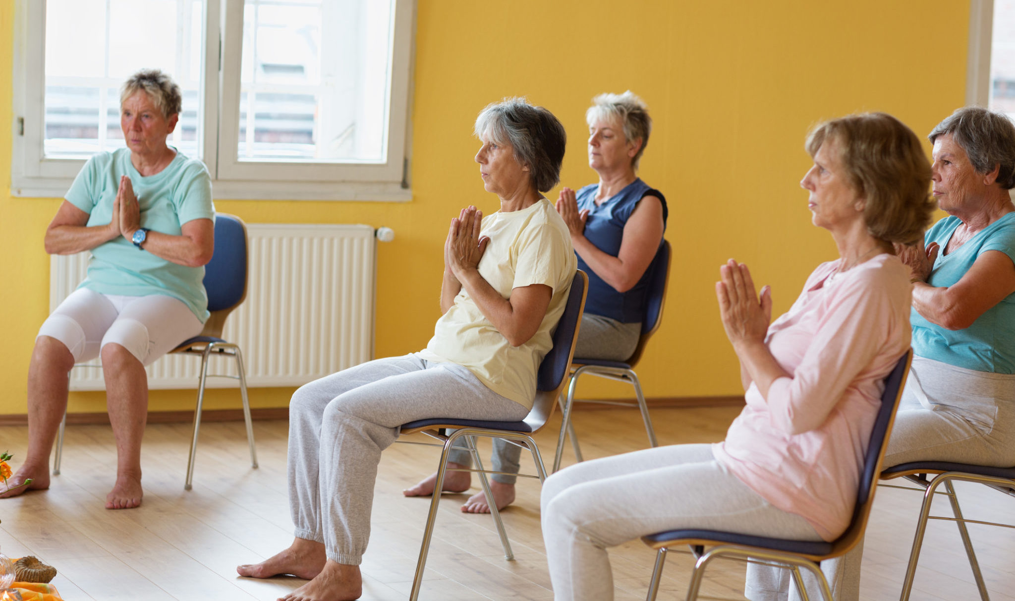 active senior women in yoga class exercisig on chairs, doing breathing exercise, hands folded