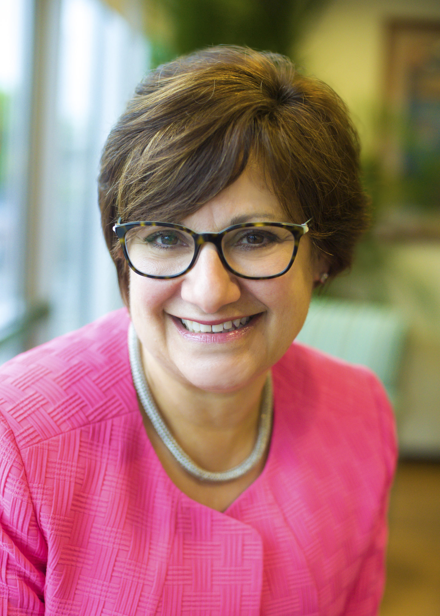 Woman in pink blazer and glasses smiling in a well-lit room