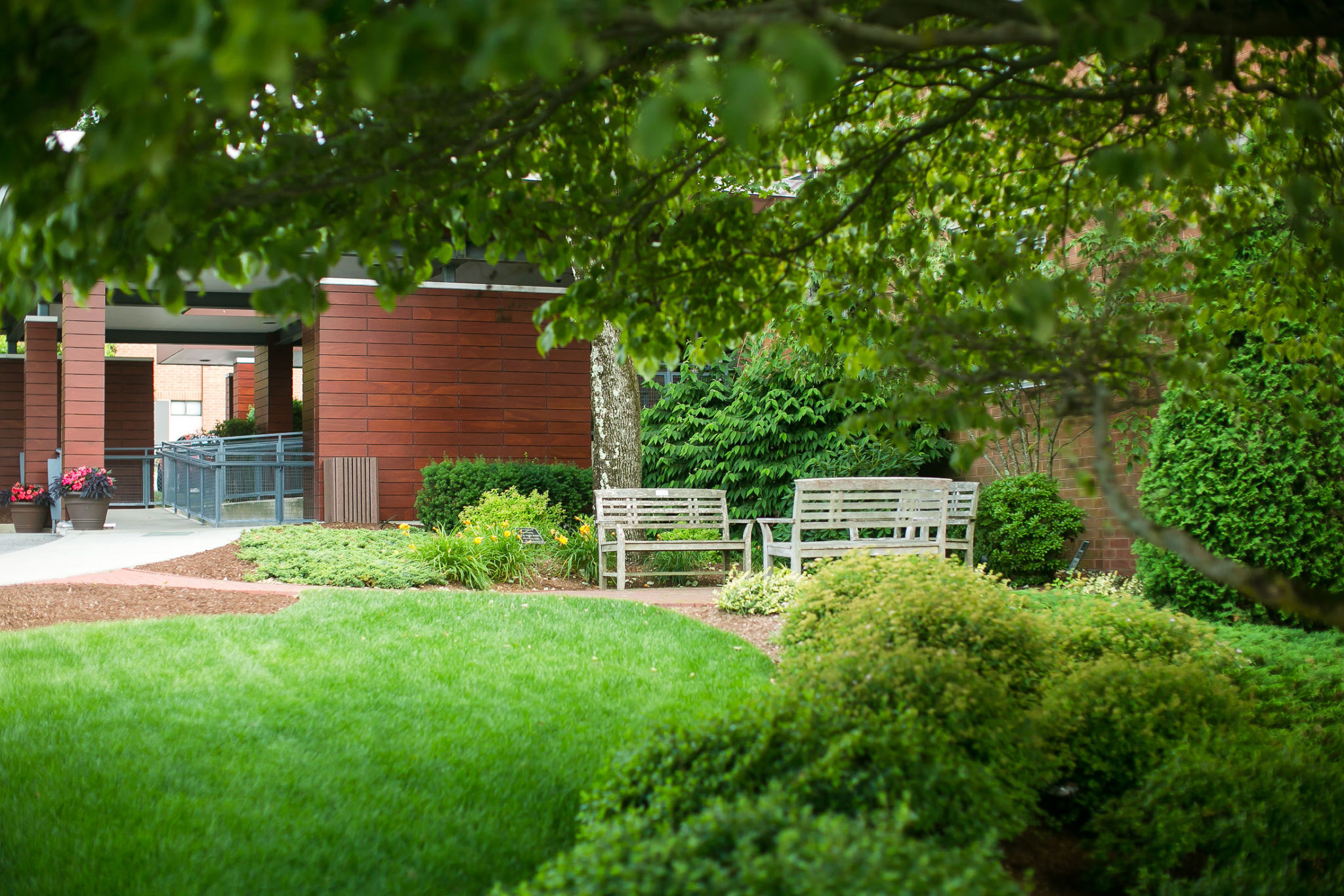 Garden with wooden benches and a brick building in the background at the hospice center