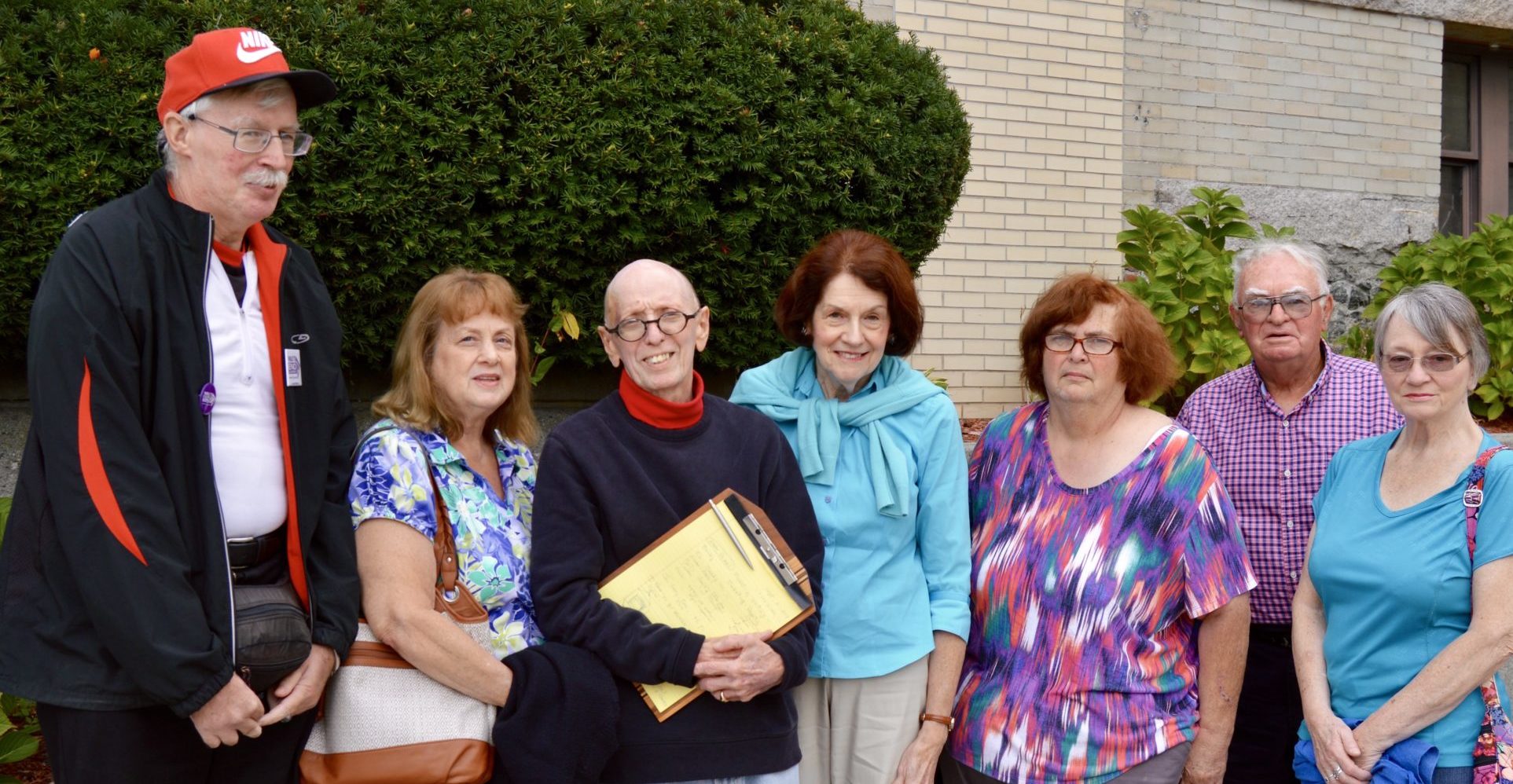 A group of three men and four women standing in front of a bush