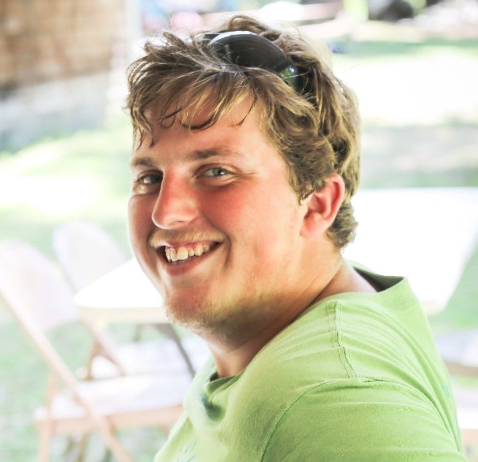 Young male with blond hair and blue eyes, wearing a green shirt and smiling