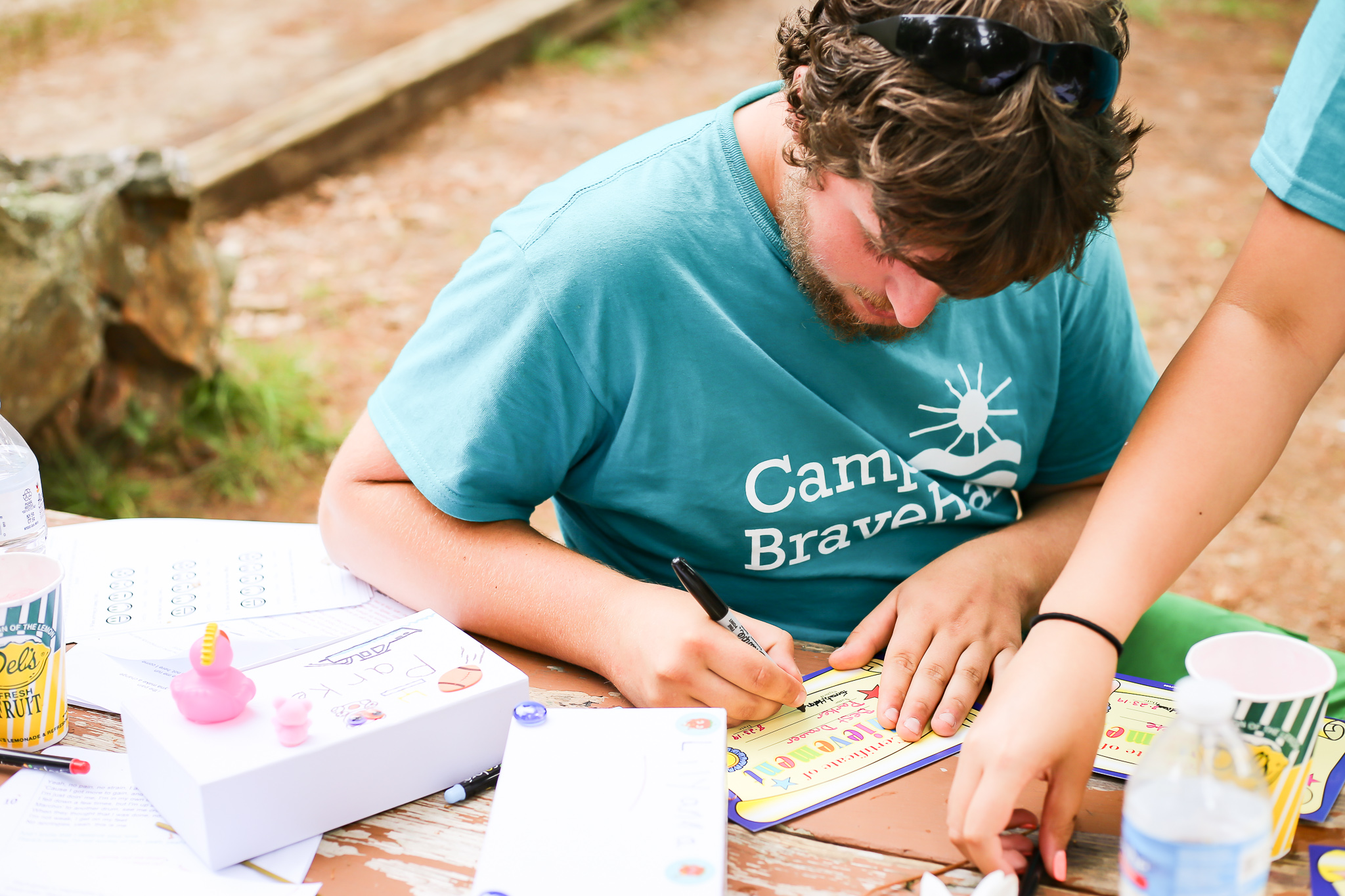 young blonde man writing on a card while sitting at a picnic table