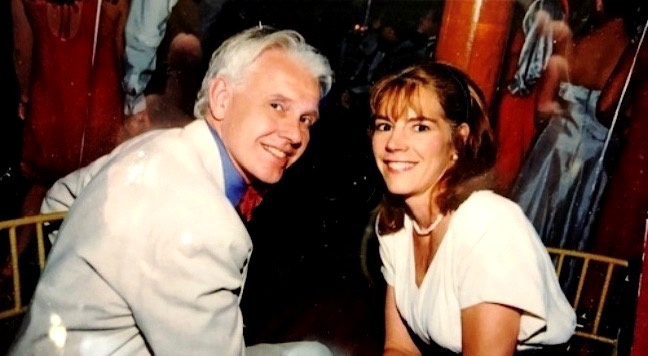 A man in a light suit at a fundraiser with his brunette well-dressed wife, both are smiling.