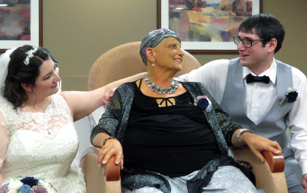Woman on hospice service looks at her son as his bride sits to the left of her
