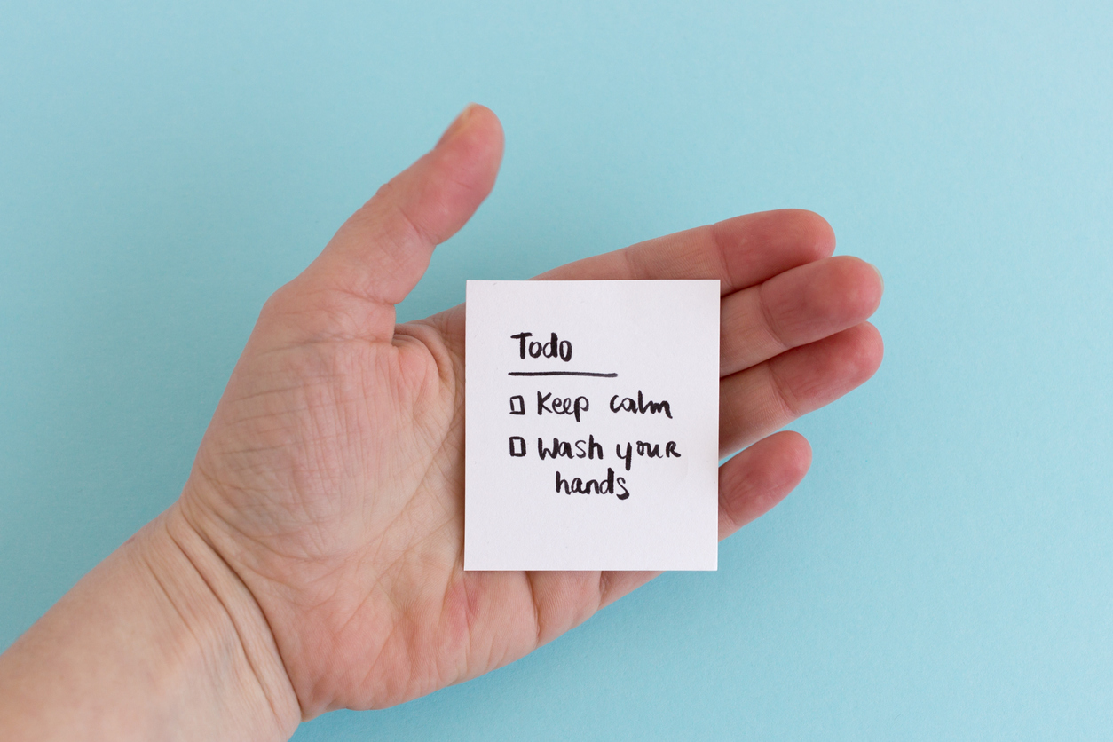 Hand holding a handwritten todo list with two reminders to stay healthy: Keep calm, wash you hands