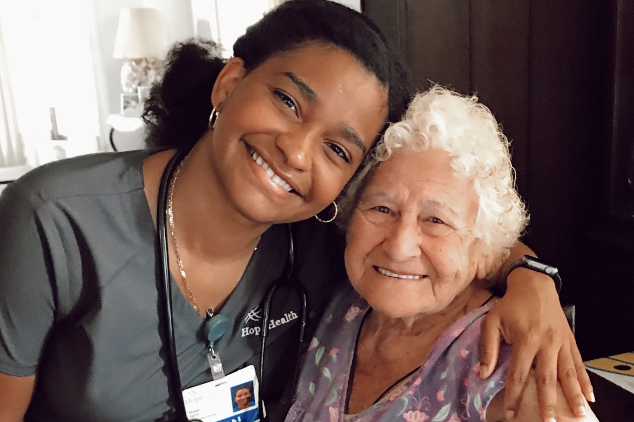 A young nurse wraps her arm around her geriatric female patient