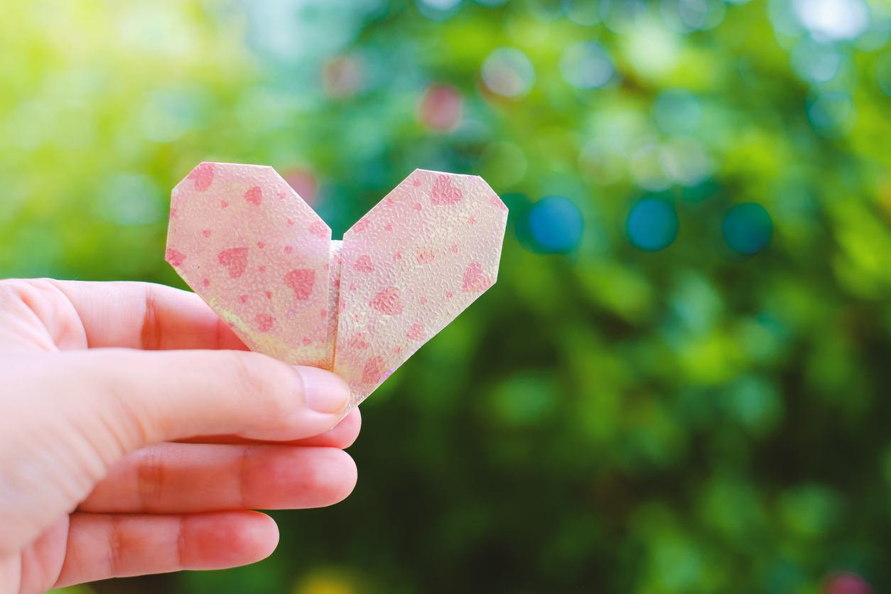 Hand holding paper heart origami on blurred green natural background for Valentine's day and love concept