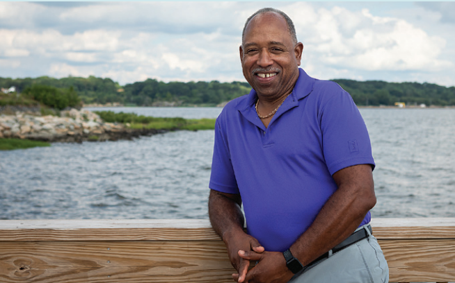 Man in purple shirt smiling while standing in front of the ocean; he is opening up about his grief experience