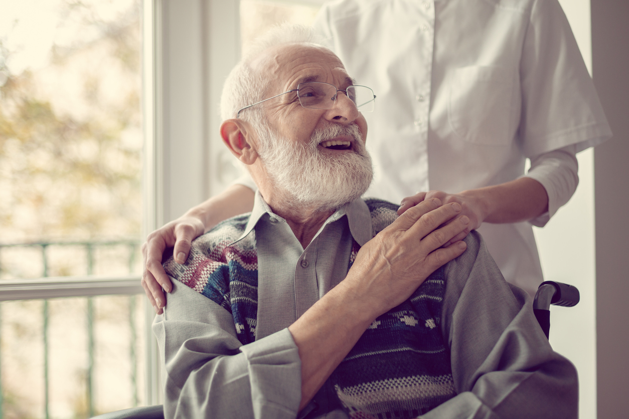 Senior man sitting on the wheelchair, laughing and holding his nurse's hand Senior man sitting on the wheelchair, laughing and holding his nurse's hand