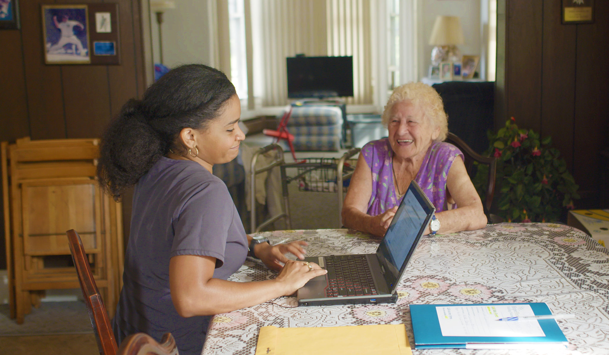 Home care nurse sitting at table with patient while updating the patients chart on a laptop