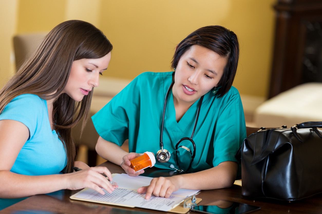 Nurse helps pregnant woman with medication at home Home heathcare nurse helps a young Caucasian pregnant woman with her medication. The woman is holding the medicine bottle and reading about possible side effects. The young Asian nurse talks with her. The nurse is wearing blue scrubs with stethoscope around her neck.