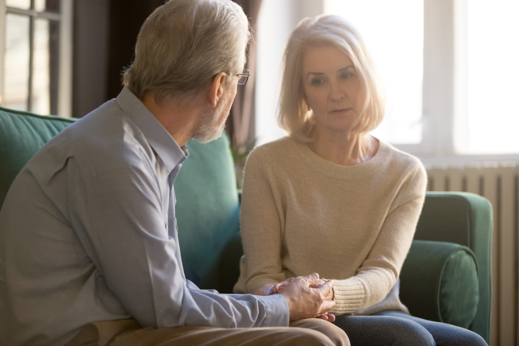 Spouses sitting on couch elderly husband comforting sad woman Sixty years old spouses sitting on couch, loving elderly husband comforting sad frustrated wife, hoary couple holds hands man demonstrates love, care and empathy, showing beloved woman support concept