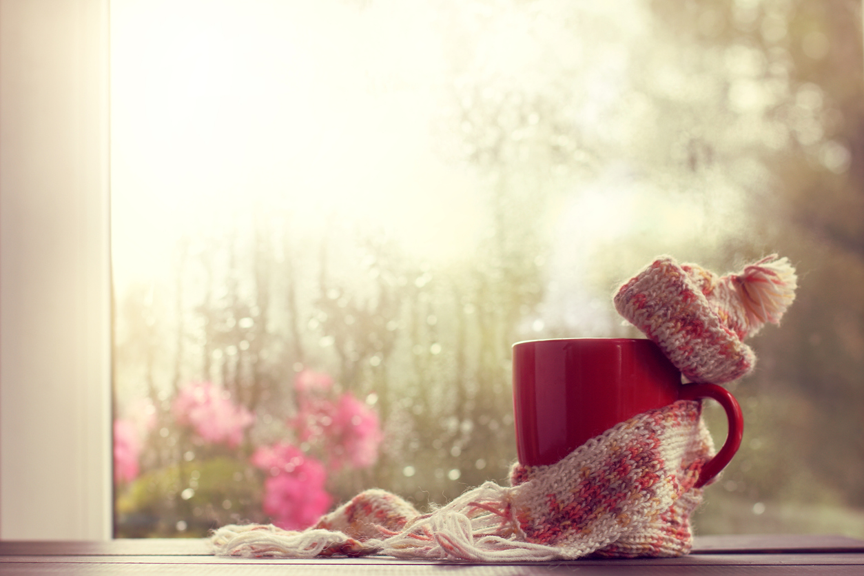 hot red mug in scarf and hat on the background window after the rain; symbolizing grief support during the holidays