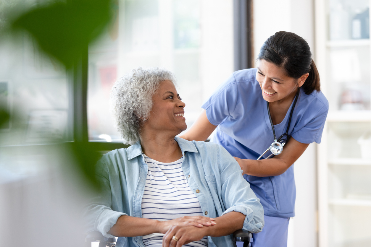 A cheerful female nurse wheels the senior woman into the examination room at the doctor's office.