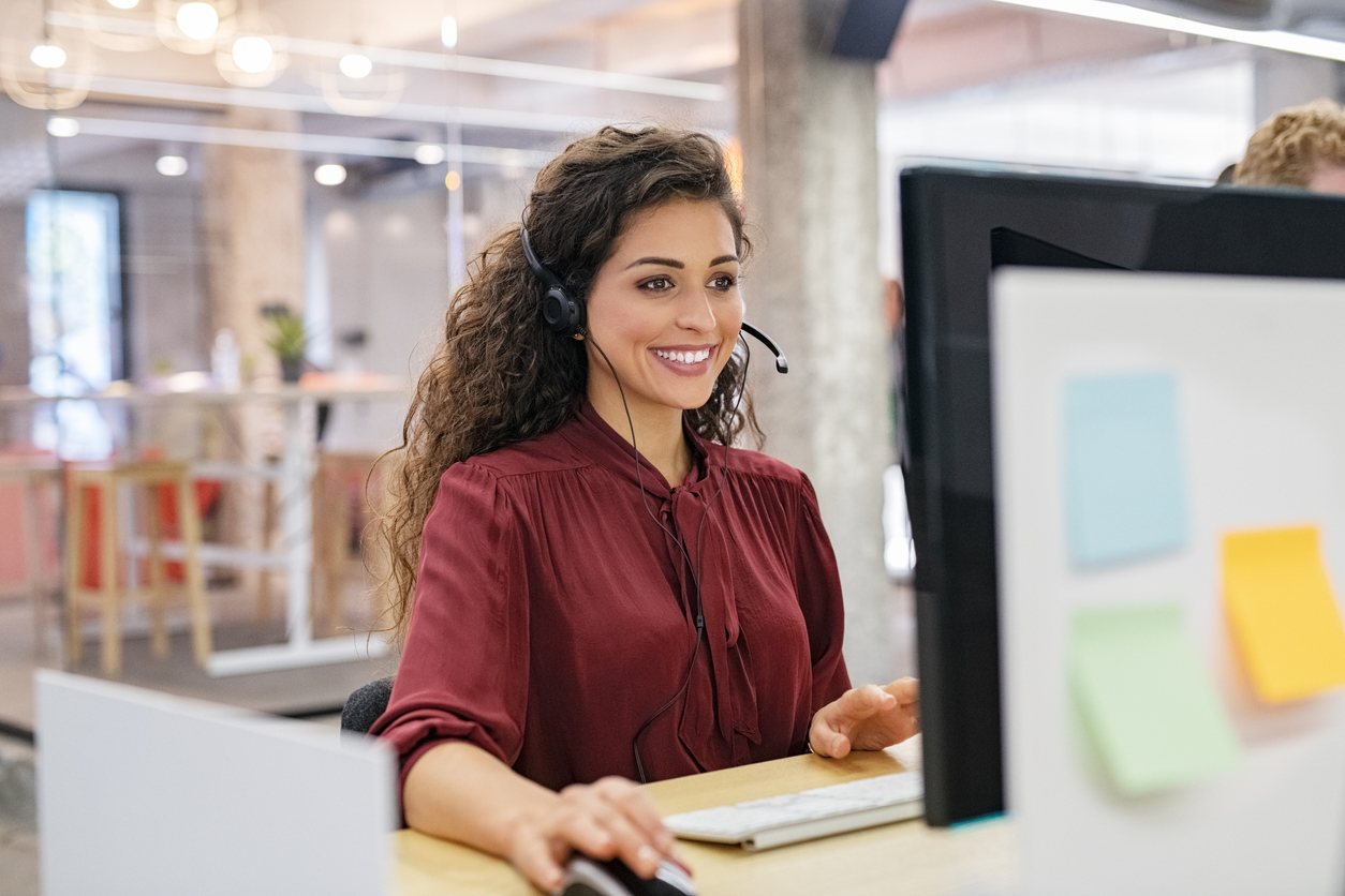 Happy smiling woman working in call center Customer support phone operator working at computer. Happy call center agent working on support hotline in office. Smiling call center agent in conversation with customer over headset.