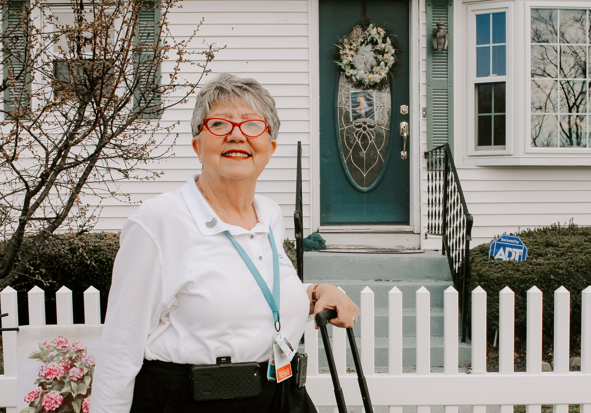Home health care occupational therapist stands in front of white picket fence before she heads into her patients home to provide care