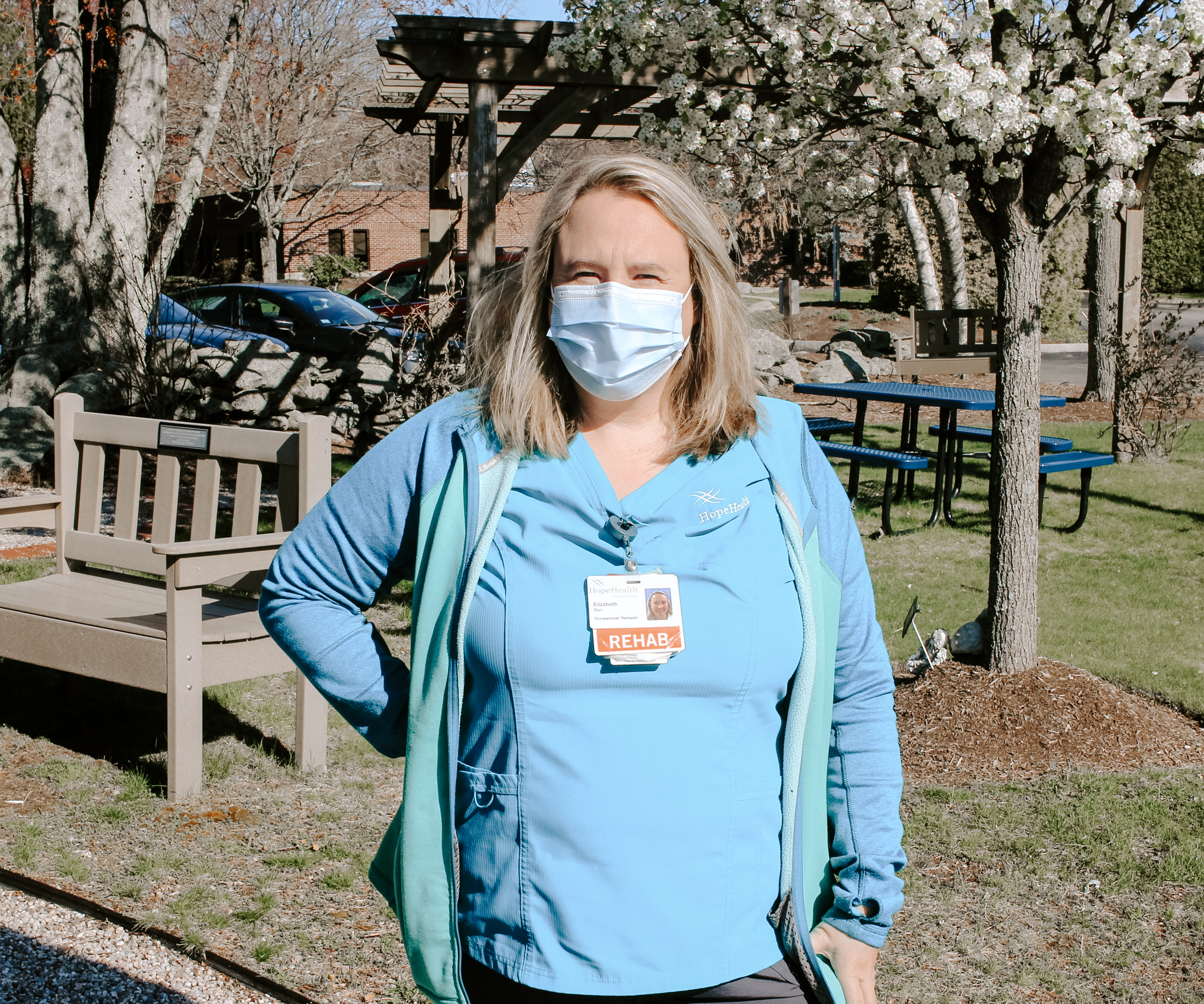 Home health care occupational therapist stands in garden wearing a surgical mask