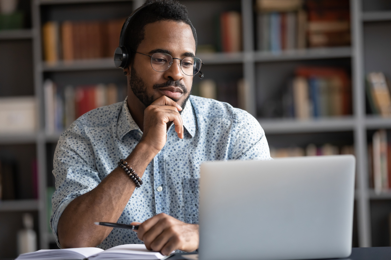 Focused African man wear headphones with microphone looking at laptop screen as he participates in a virtual grief support group through HopeHealth