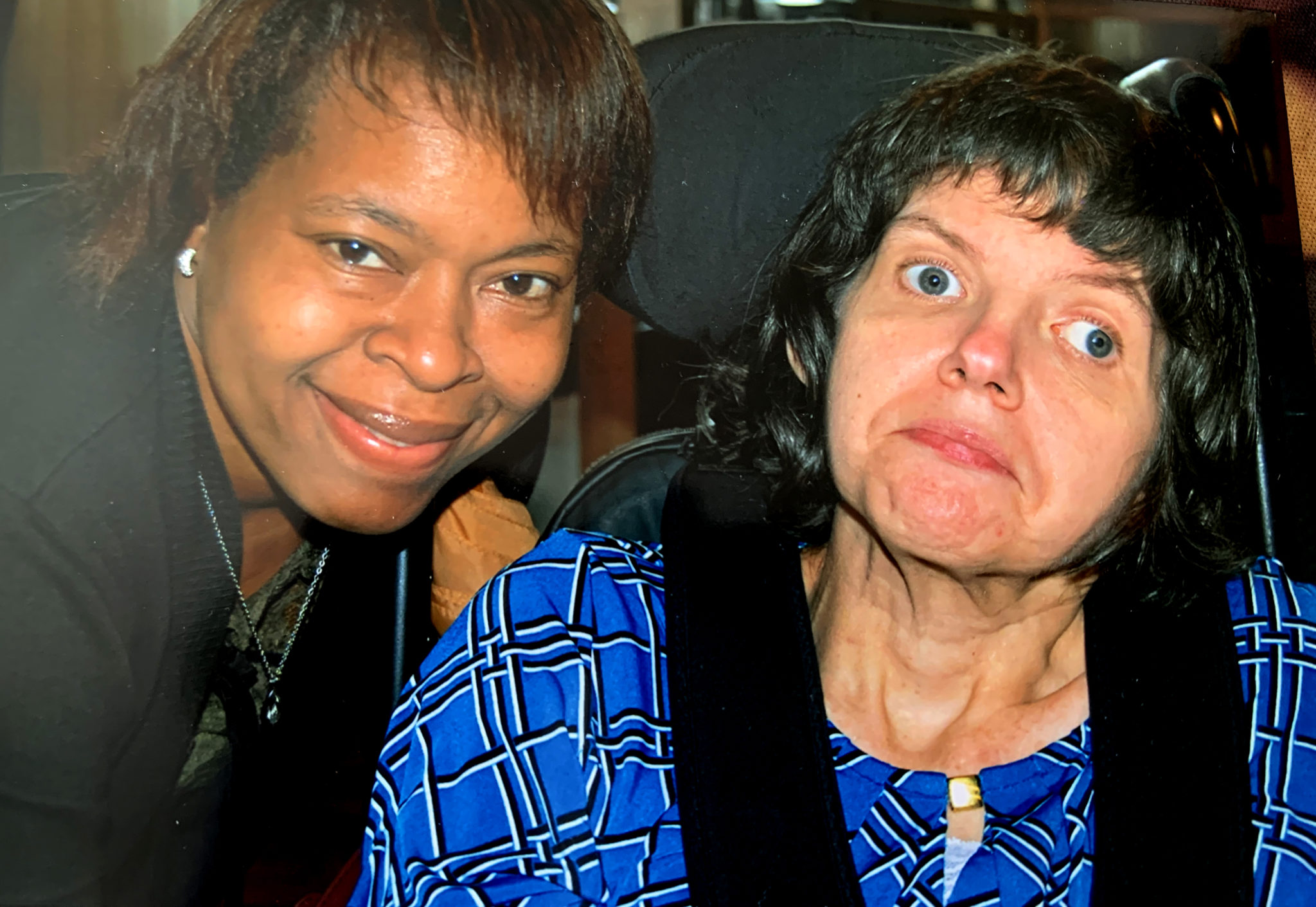 African-American woman who is a hospice aide on left and woman who is a hospice patient in a wheelchair is on right