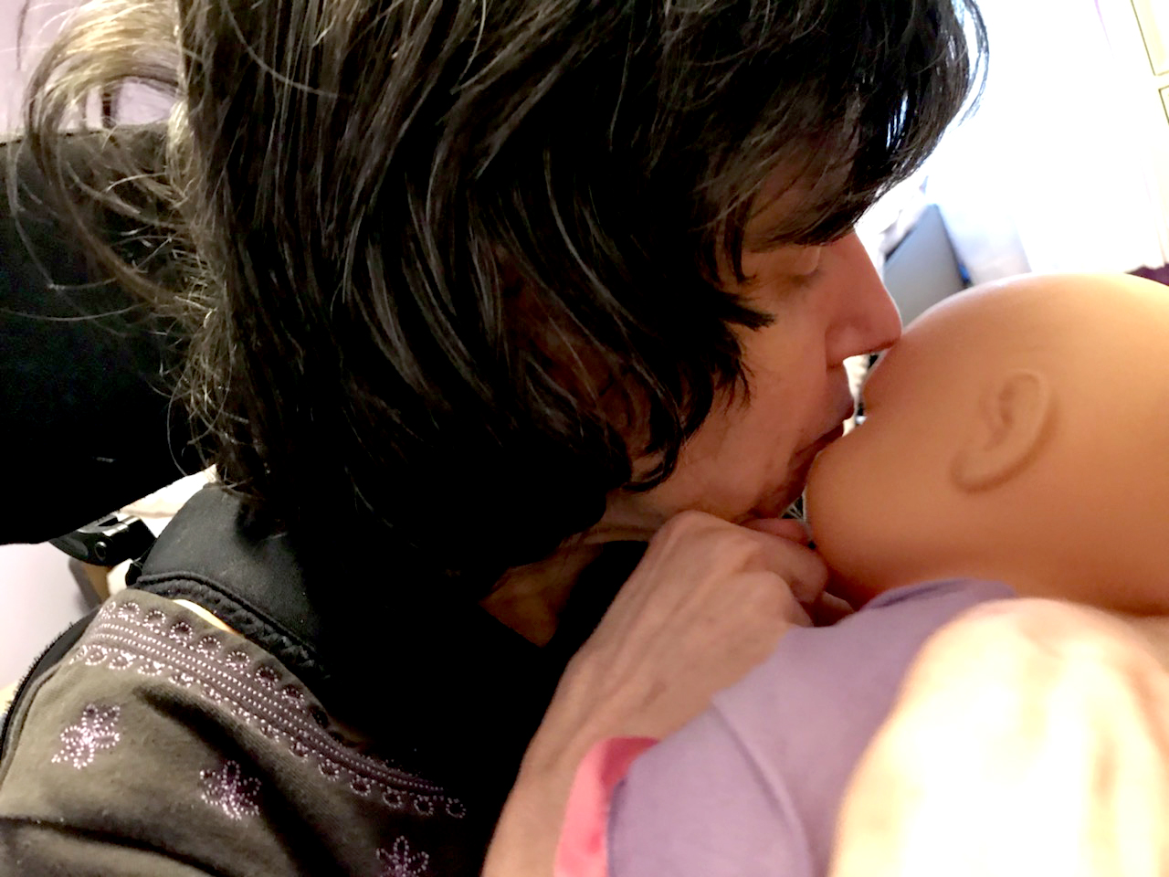 Woman with dark hair gently kisses baby doll