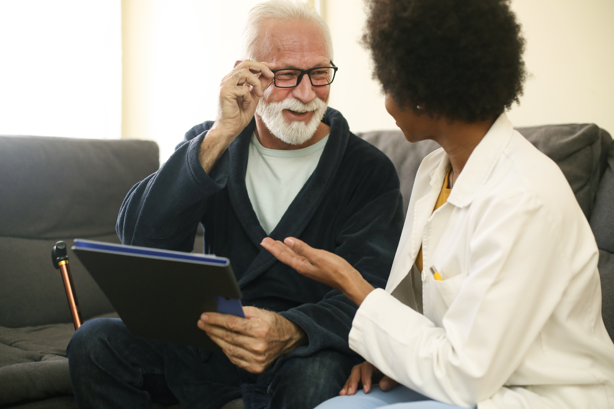 Senior man with a female doctor at his home. About 70 years old Caucasian male and a 35 years old African female.
