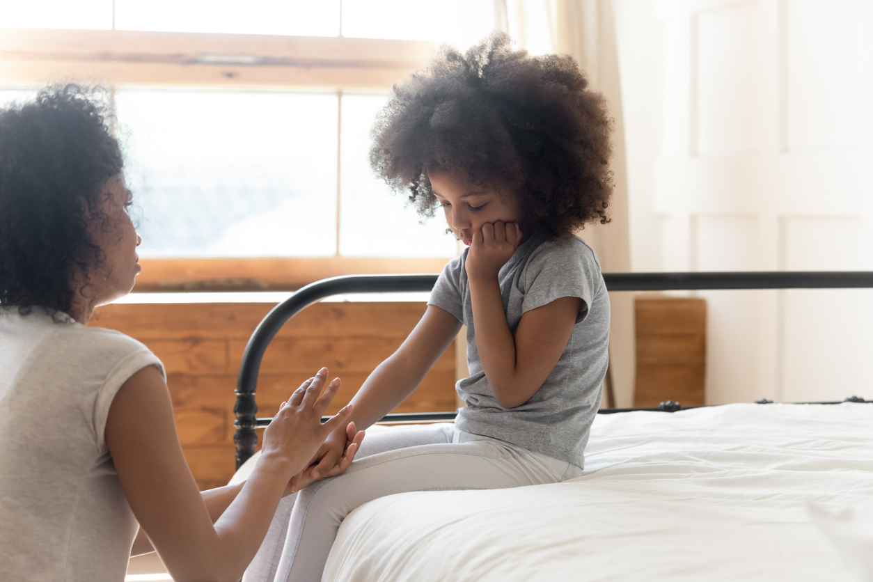 Mom reaching out to talk to her daughter who is sitting on her bed, offering grief support