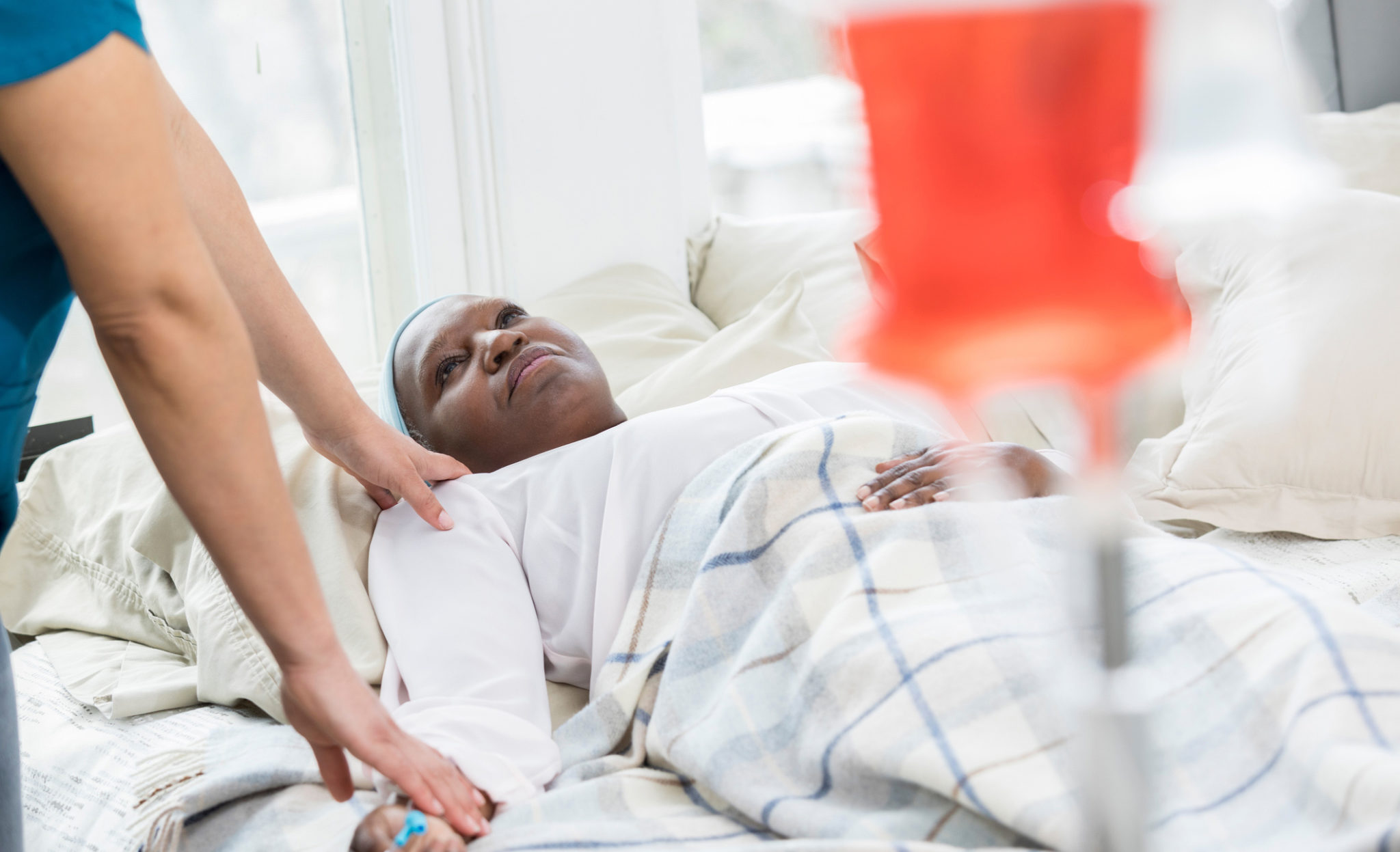 Hospice nurse checks on senior female patient Unrecognizable hospice nurse cares for a senior woman. The patient is lying in bed. An iv drip is in the foreground.
