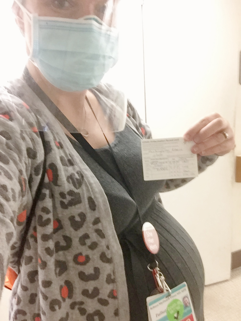 Pregnant hospice and palliative care doctor proudly holds up her COVID-19 vaccine card