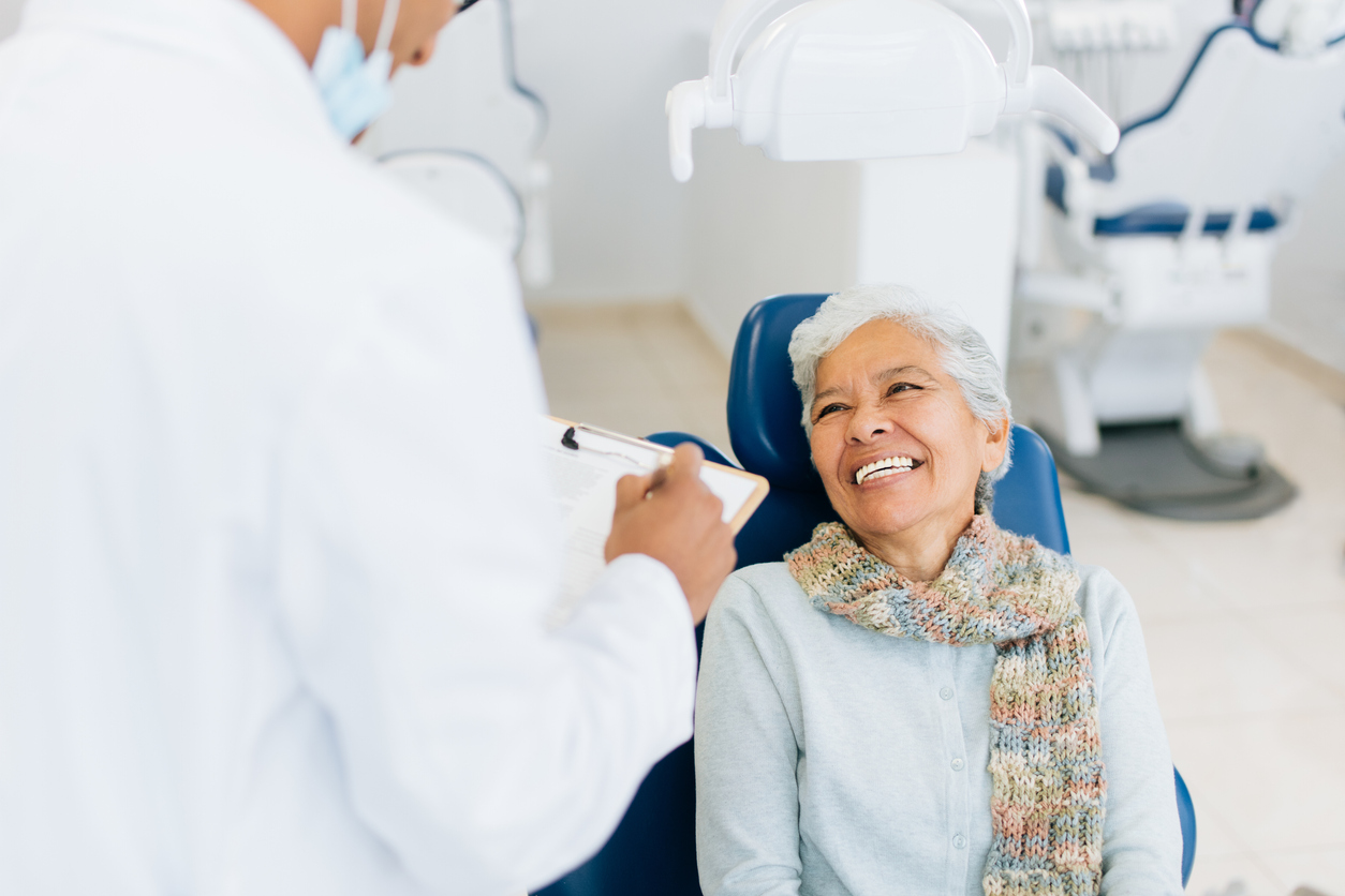 A happy senior female patient sitting on dental examination chair, looking at the male dentist and smiling.