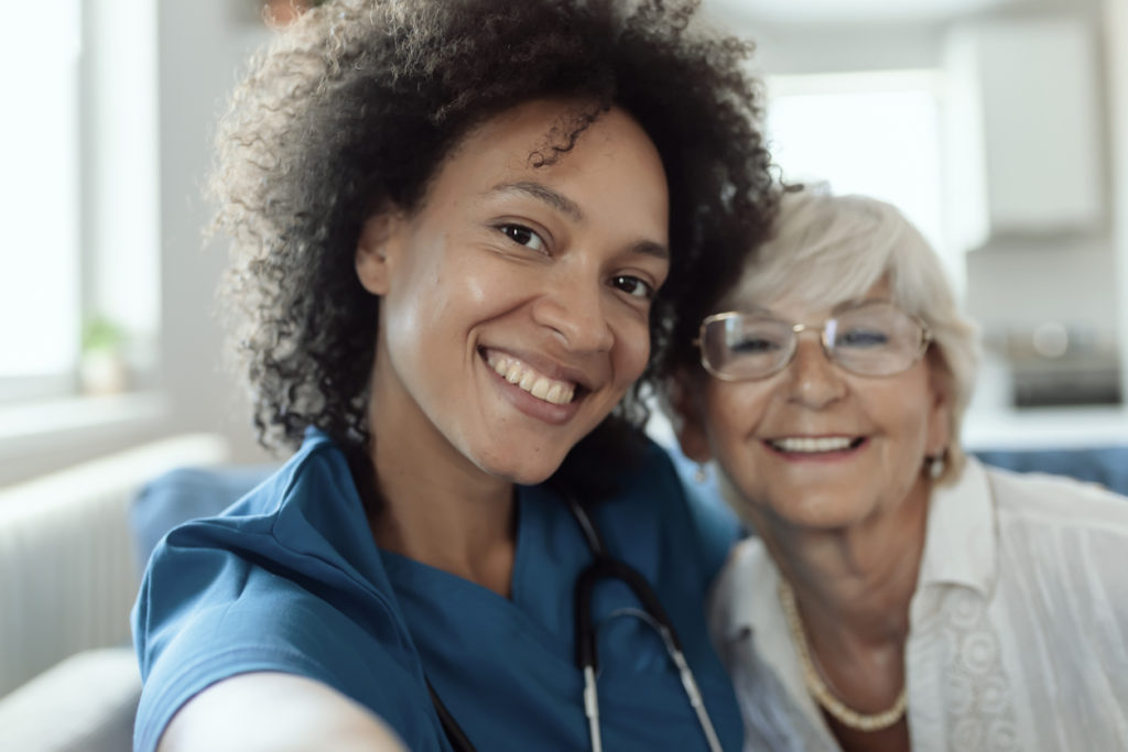 Female Mixed Race Nurse and Elderly Patient Taking a Selfie to Send It to the Relatives to Show That Everything is Going Well. Happy Elderly Patient and Female Doctor Making Selfie Photo in the Nursing Home Spending Time Together.