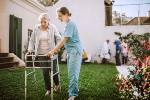 Female physical therapist helping senior woman with mobility walker at nursing home