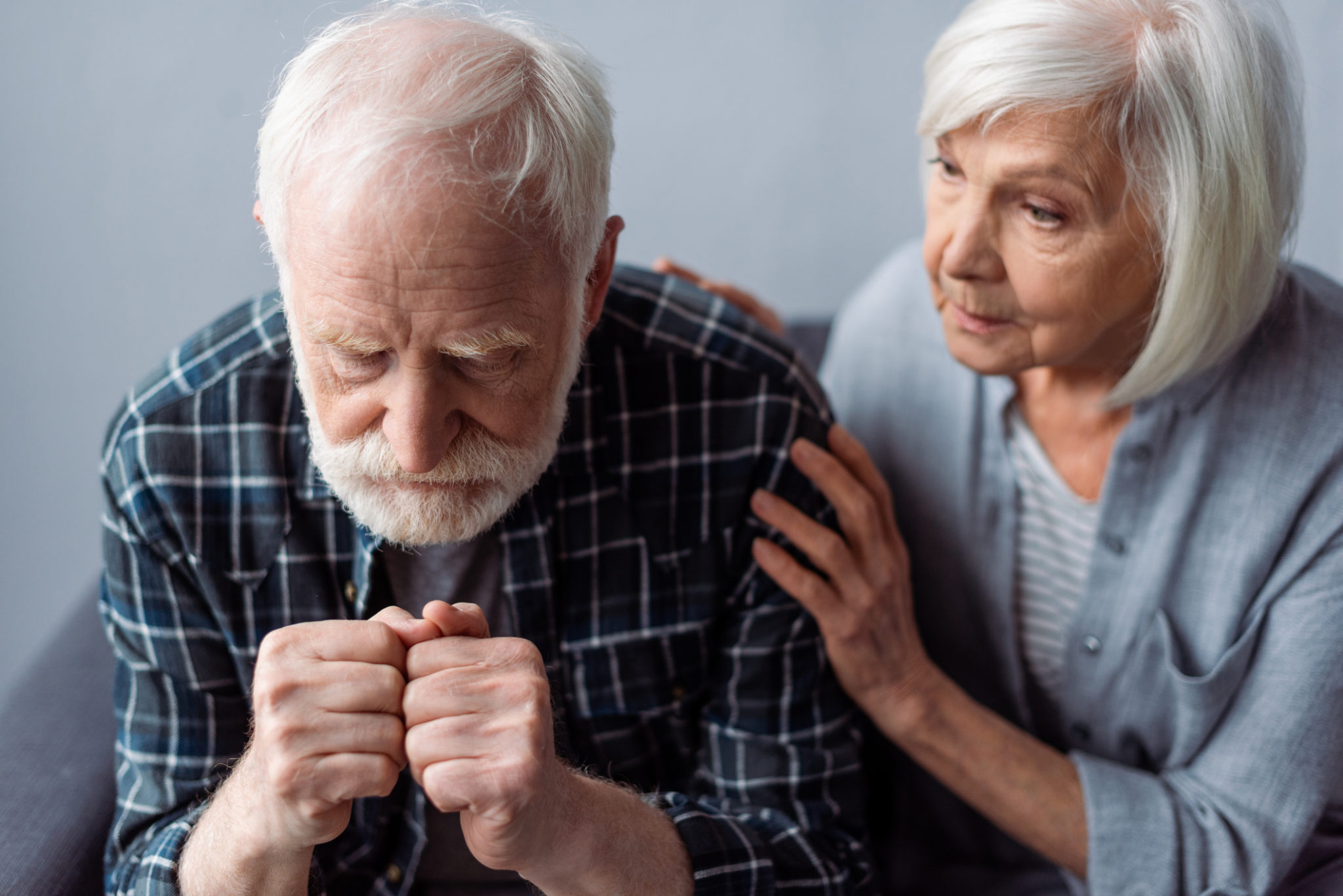 worried senior woman touching husband suffering from dementia and sitting with clenched fists worried senior woman touching husband suffering from dementia and sitting with clenched fists