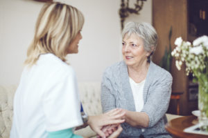 Mid adult blonde nurse is consulting with a senior lady on a sofa. Candid shot.
