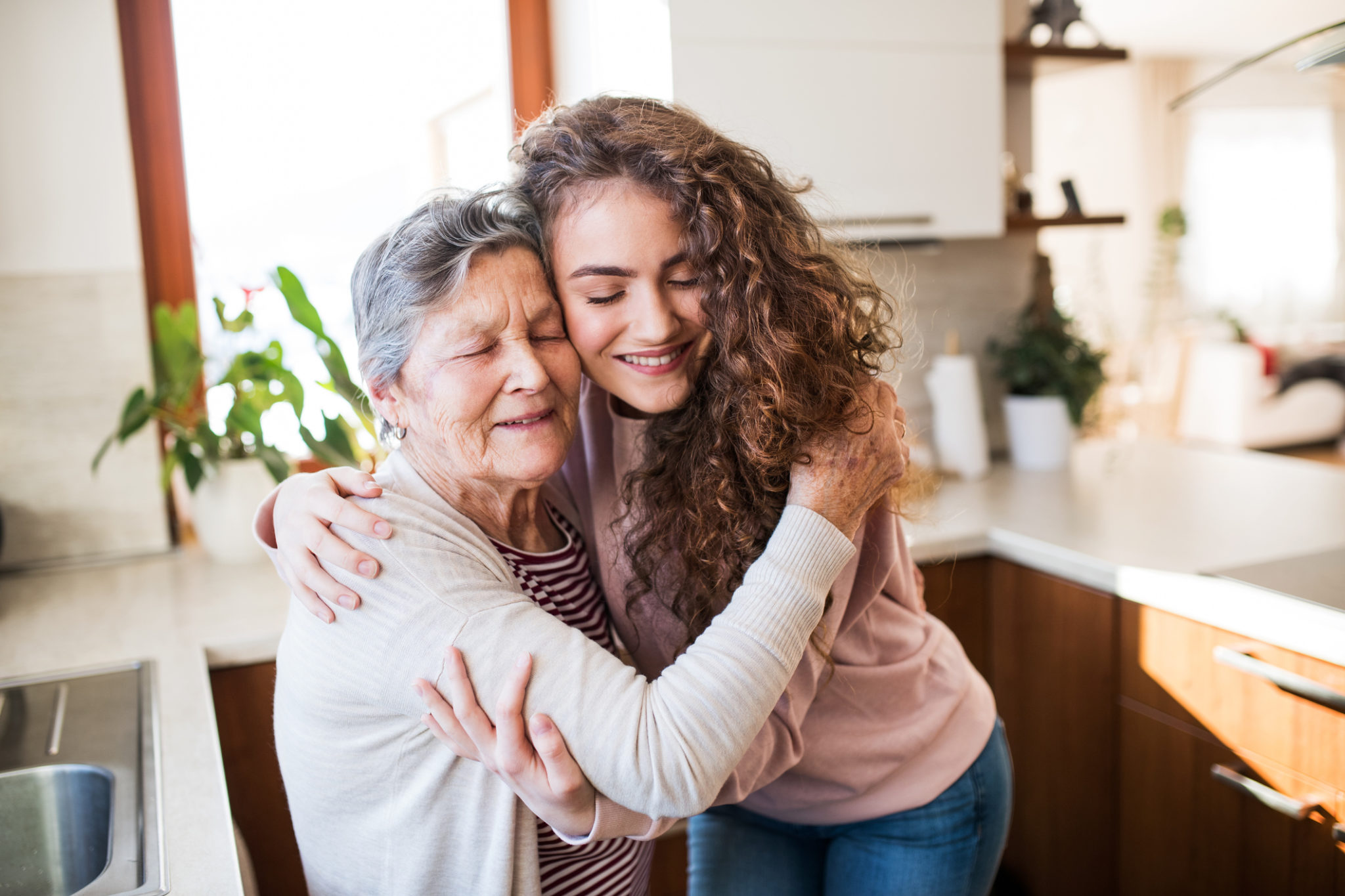 A teenage girl with grandmother at home, hugging. A teenage girl with grandmother at home, hugging. Family and generations concept.