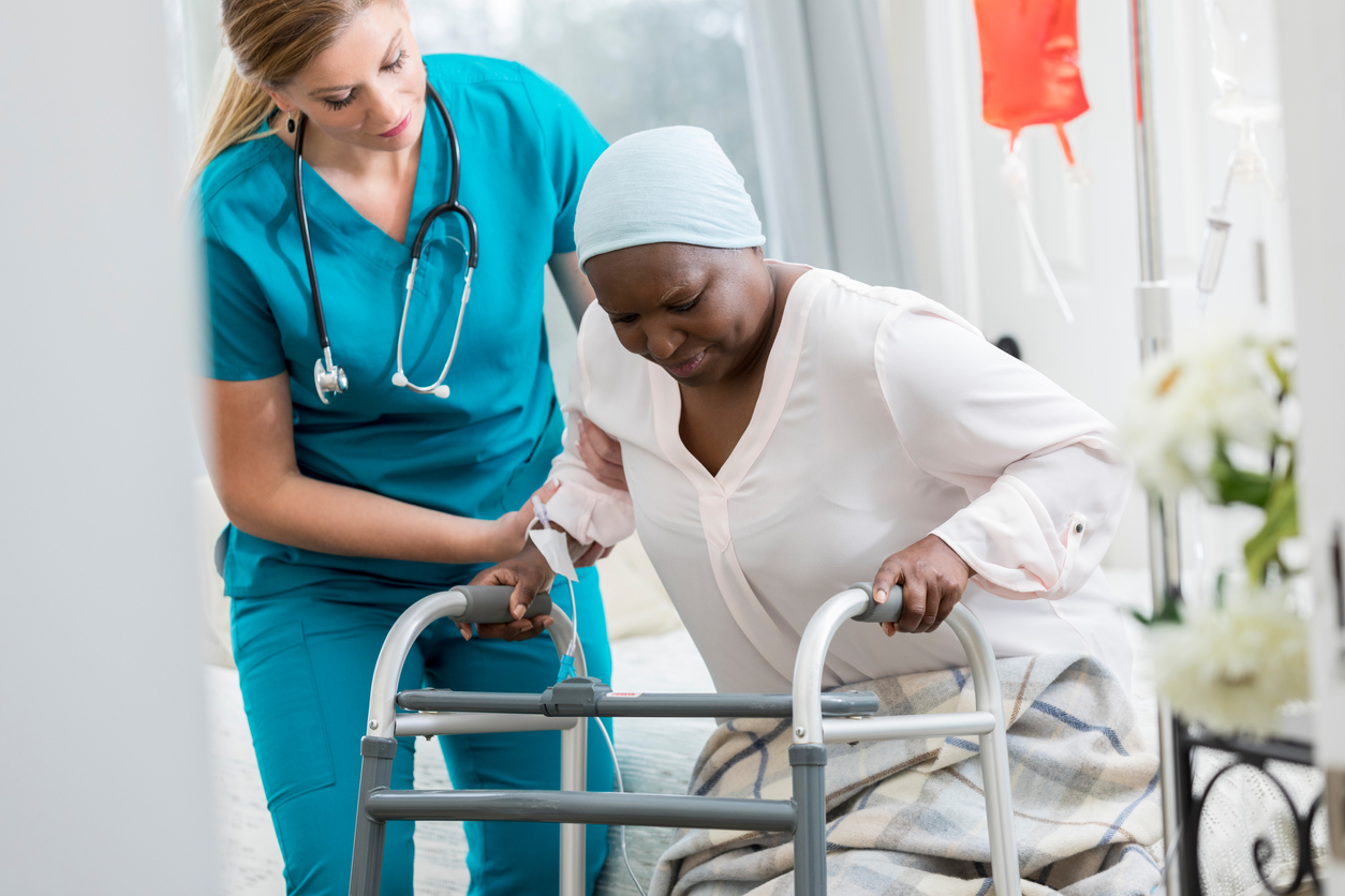 Senior African American female patient uses a walker in her home. A home healthcare nurse is assisting her.